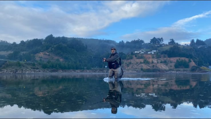Pescador del club en el mar con marea baja, usando caña spinner